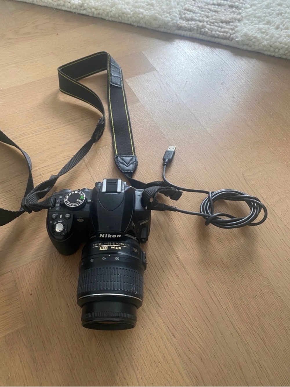Nikon 3100 black DSLR with zoom lens and attached USB cable